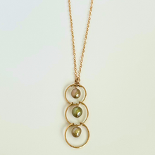 Load image into Gallery viewer, Gold necklace with three circular pendants and green pearls on a light background