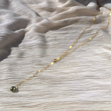 Load image into Gallery viewer, A gold-filled paperclip chain lariat necklace with a green fresh water pearl at the end, displayed on a textured white background.